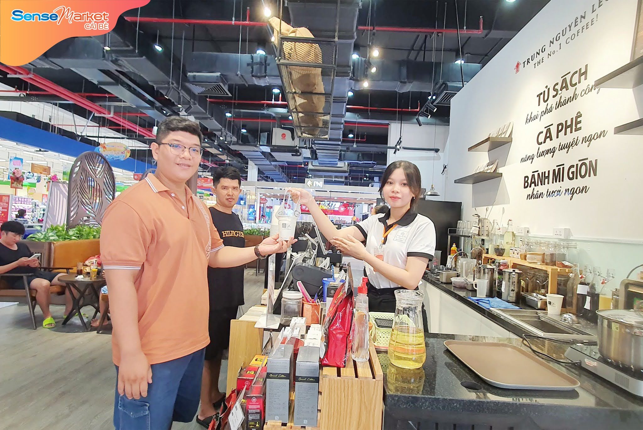Khách hàng nhận đồ uống từ nhân viên tại quầy cà phê trong SenseMarket Cái Bè